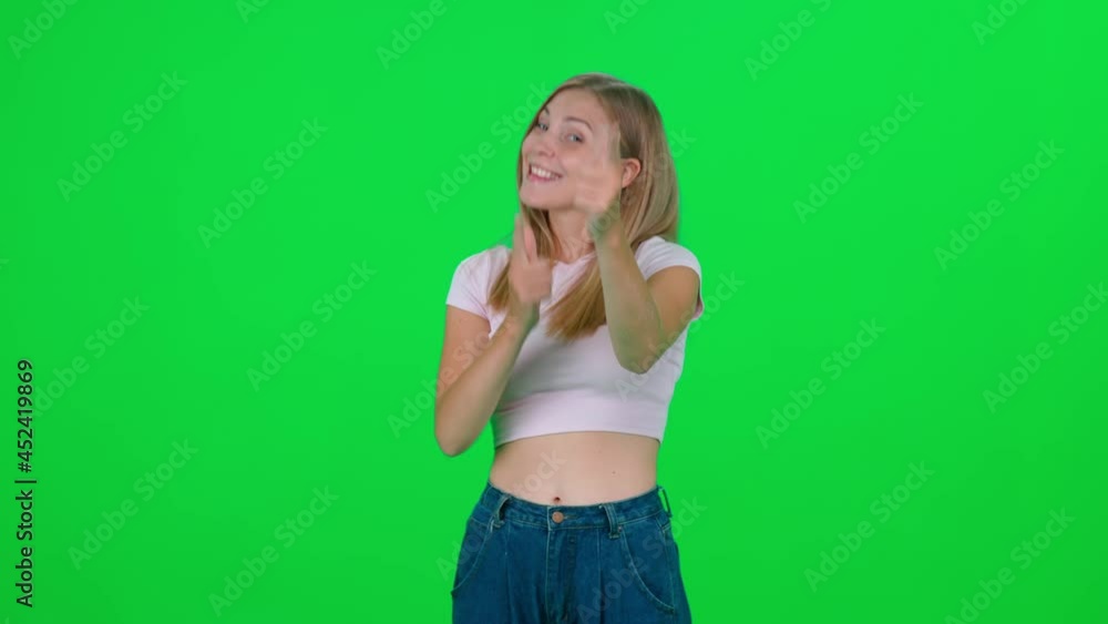 Caucasian female standing in green room and looks at the camera, chroma key background, the young blonde woman points at the viewer and smiles, positive emotions. Caucasian female standing in green room and looks at the camera, chroma key background, the young blonde woman points at the viewer and smiles, positive emotions.