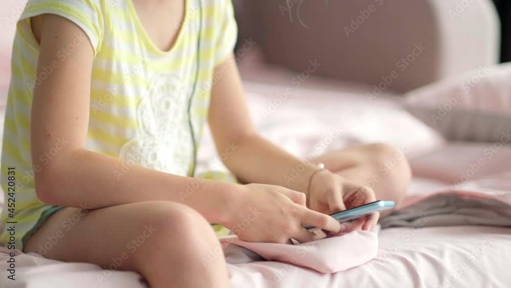 Little girl using mobile phone at home. Close up child hands with smartphone pressing finger, reading social media internet, chatting, typing text or shopping online. Mobile phone in two hands Little girl using mobile phone at home. Close up child hands with smartphone pressing finger, reading social media internet, chatting, typing text or shopping online. Mobile phone in two hands