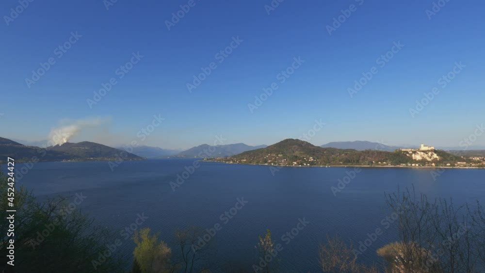 Panoramic view over Maggiore lake and smoke from mountain due to burning fire close to Nebbiuno in Piedmont, Italy. Zoom in Panoramic view over Maggiore lake and smoke from mountain due to burning fire close to Nebbiuno in Piedmont, Italy. Zoom in