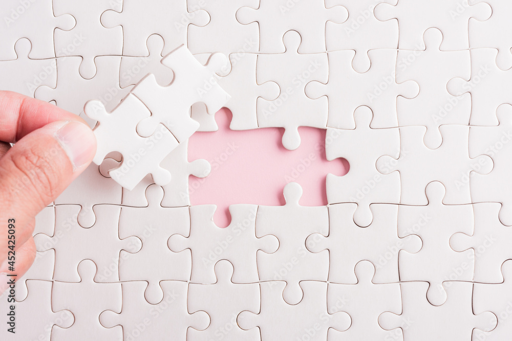 Top view flat lay of hand-holding last piece white paper jigsaw puzzle game last pieces put to place for solve problem complete mission, studio shot on a pink background, quiz calculation concept Top view flat lay of hand-holding last piece white paper jigsaw puzzle game last pieces put to place for solve problem complete mission, studio shot on a pink background, quiz calculation concept