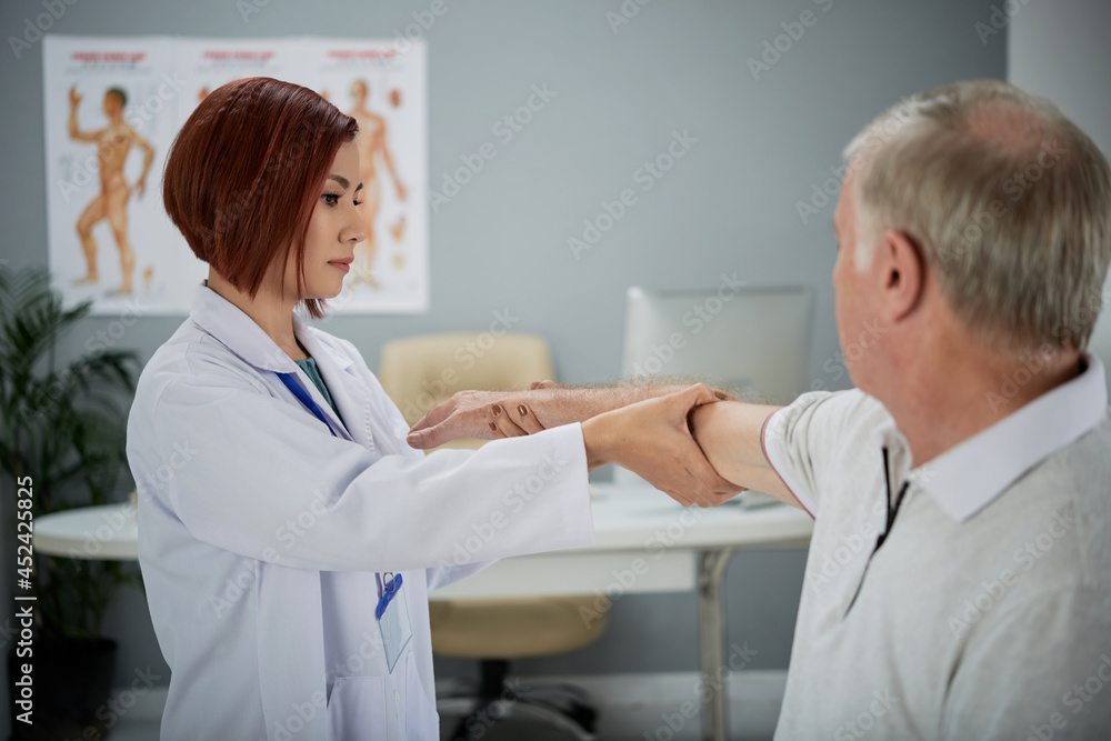 Serious physiotherapist asking senior patient to stretch out arm when she is checking his injury Serious physiotherapist asking senior patient to stretch out arm when she is checking his injury