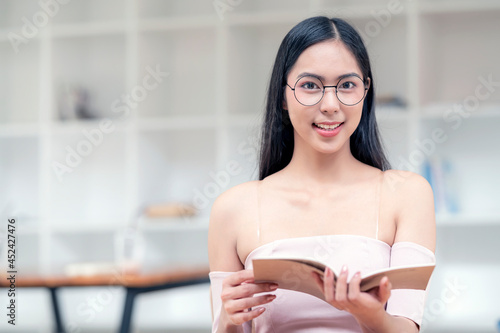 Free Download Portrait of young beautiful asian woman with glasses holding book, smiling and looking at camera, closeup view. - GFXLoad