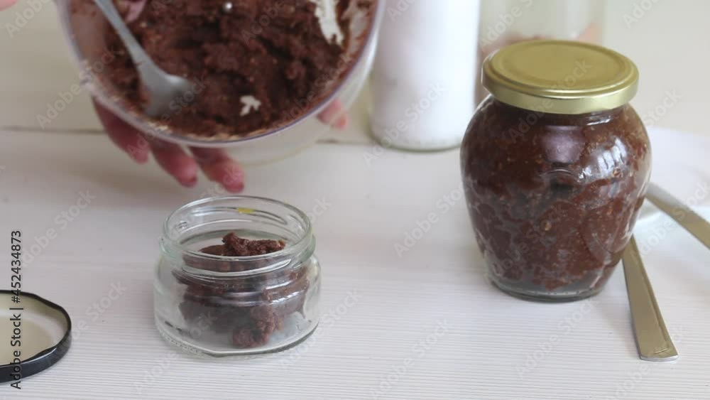 A woman puts nut butter from a blender bowl into a jar. Walnut urbech