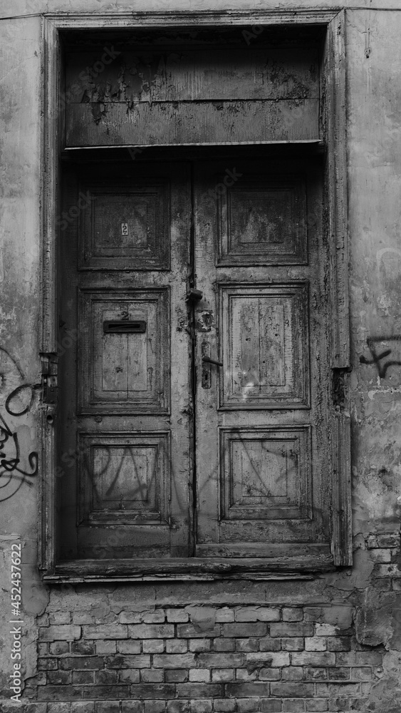 Black and white photo of a closed old wooden door with cracked paint in a house in old Riga Black and white photo of a closed old wooden door with cracked paint in a house in old Riga