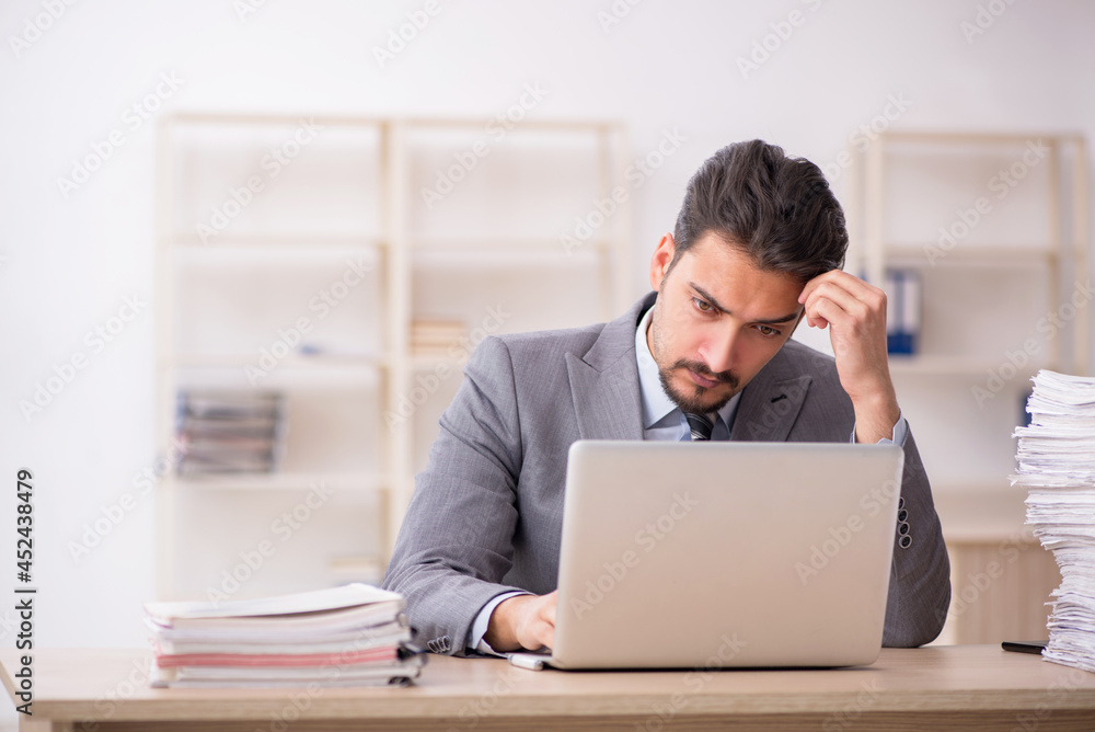 Young male employee unhappy with excessive work in the office Young male employee unhappy with excessive work in the office