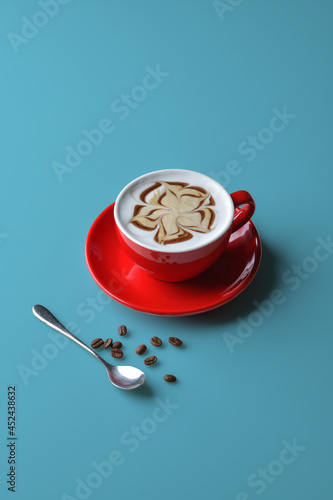 Latte coffee in red mug decorated with caramel and chocolate motifs. put a glass on the blue background