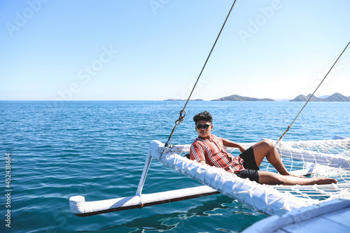 Asian man wearing sunglasses relaxing on catamaran net enjoying summer time