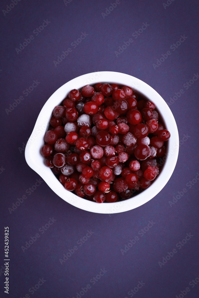 Frozen cranberry in white bowl on violet background. Selective focus. Flat lay of frozen cranberries. Frozen cranberry in white bowl on violet background. Selective focus. Flat lay of frozen cranberries.