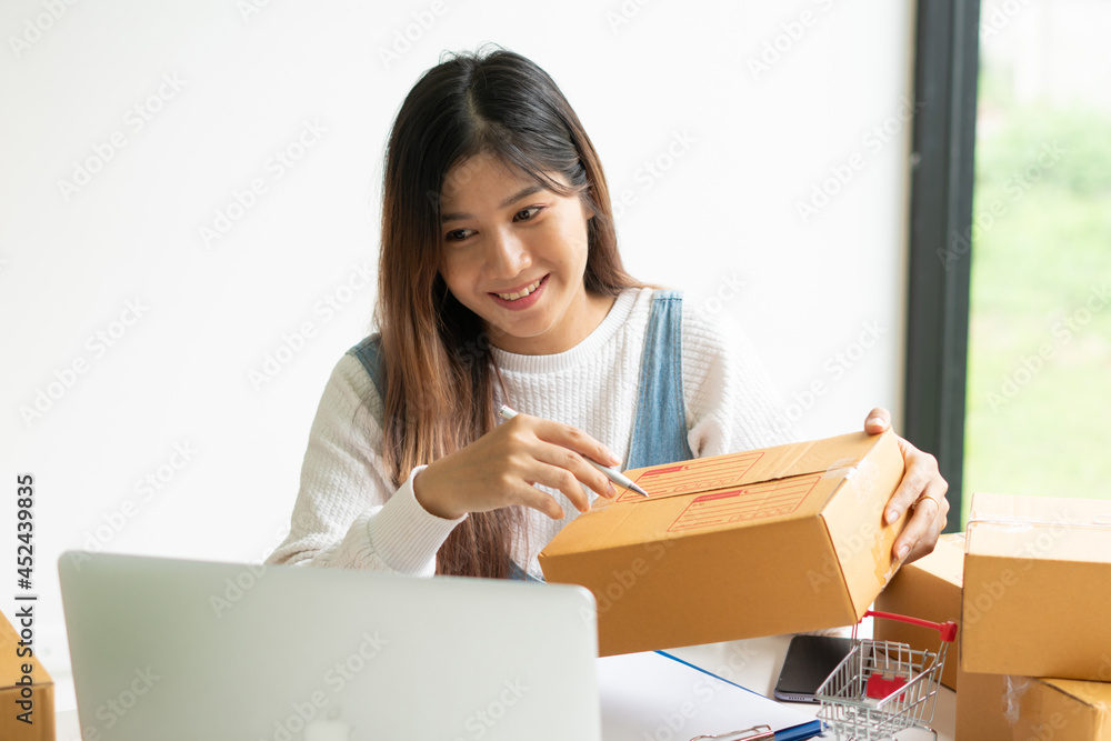 Young smiling beautiful owner asian woman freelance sme business online shopping working on laptop computer with parcel box on desk at home - SME business online and delivery concept Young smiling beautiful owner asian woman freelance sme business online shopping working on laptop computer with parcel box on desk at home - SME business online and delivery concept