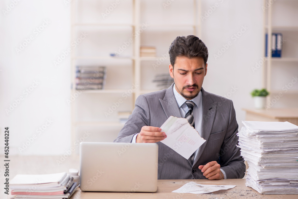 Young male employee unhappy with excessive work in the office Young male employee unhappy with excessive work in the office