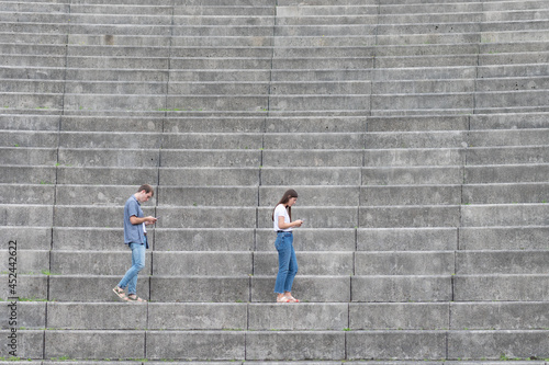 Man and woman with digital addiction walking on the stairs of a grandstand and looking to their phones in bad physical posture.