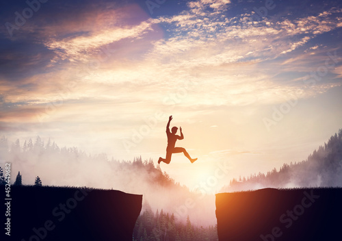 Man jumping between cliffs at sunset.