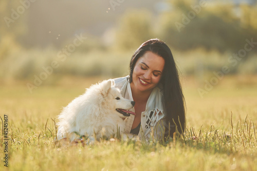 Laying down on the ground. Woman with her dog is having fun on the field at sunny daytime