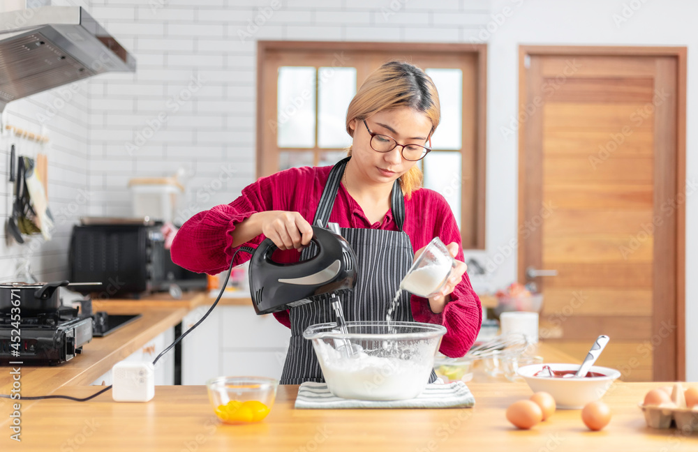 Asian girl using the blender, blend dough and other ingredients for cooking the chocolate cake with happy feeling in the kitchen room. Asian girl using the blender, blend dough and other ingredients for cooking the chocolate cake with happy feeling in the kitchen room.