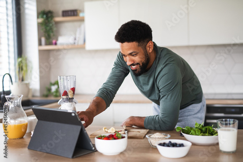Young man with tablet preparing healthy breakfast indoors at home, home office concept.