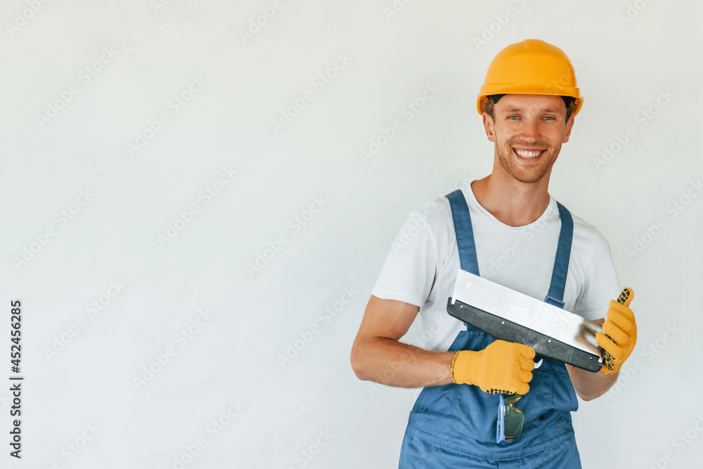 Standing near white wall. Young man working in uniform at construction at daytime Standing near white wall. Young man working in uniform at construction at daytime