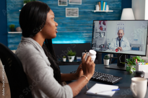 African american student discussing sickness symptoms with doctor during online videocall meeting conference telemedicine. Therapist explaining pills treatment after disease diagnosis test results photo