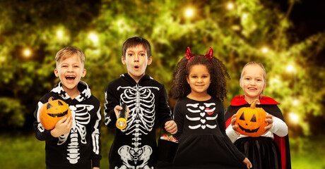 holiday and childhood concept - happy children in halloween costumes trick-or-treating over lights at night garden background