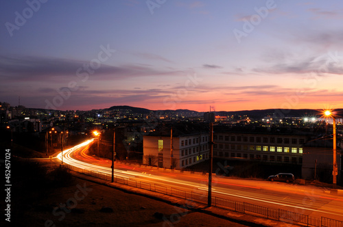 Night city Murmansk, view from the Lighthouse. Beautiful pink sky against the background of burning lights. Long bright stripe from the car. Trail of light on the road from headlights.