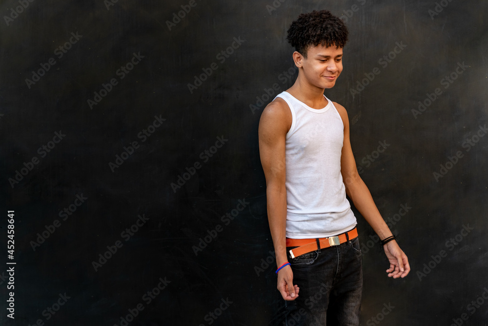 Afro latin male teenager smiling against a black wall Afro latin male teenager smiling against a black wall