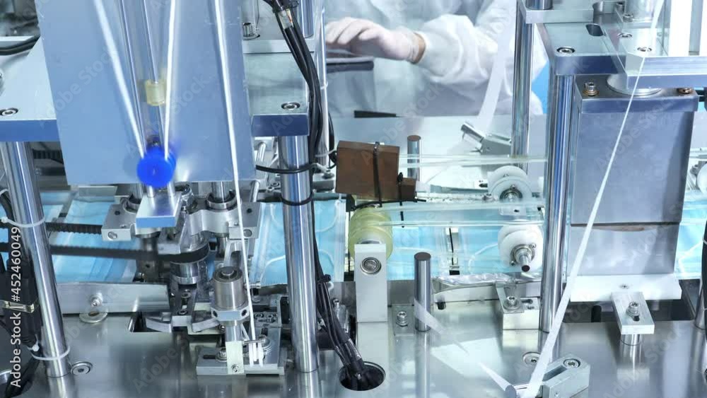 4K Production line of disposable medical face mask working in modern factory. Protective face mask moving on conveyor belt in production machine. Covid-19 pandemic protection and manufacture concept. 4K Production line of disposable medical face mask working in modern factory. Protective face mask moving on conveyor belt in production machine. Covid-19 pandemic protection and manufacture concept.