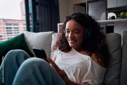 Mixed race female teen relaxing on couch listening to music with heaphones