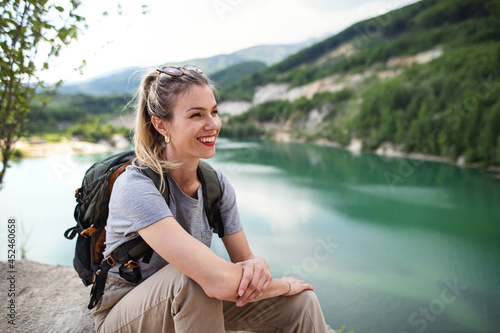 Mid adult woman tourist on hiking trip on summer holiday, resting by lake.