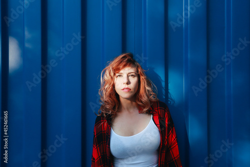 woman with bright eyes and plaid shirt leaning on a blue container outdoors