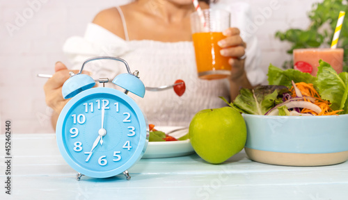 Close up of blue clock it timer for  woman restricted eating. Healthy foods between clock hands, daily eating window, fasting period, weight loss concept photo