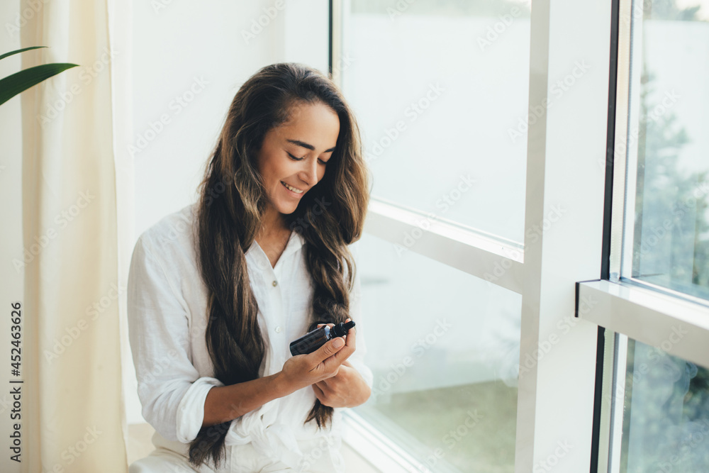 Young woman applying natural organic essential oil on hair and skin. Home spa and beauty rituals. Young woman applying natural organic essential oil on hair and skin. Home spa and beauty rituals.