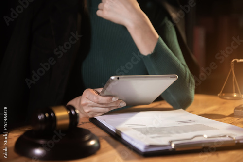 Justice and law concept.Male judge in a courtroom the gavel, working with digital tablet computer on wood table.