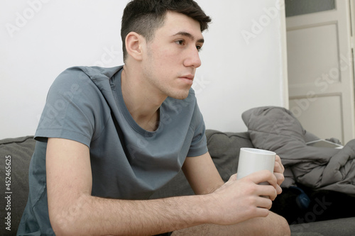 Caucasian boy on sofa sitting facing forward with cup of coffee in hand