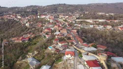 Picturesque aerial view of small Georgian town of Sighnaghi with similar terracotta roofs of houses on steep hill near Gombori Range on spring day, Kakheti  photo