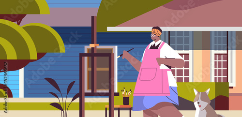 senior african american woman artist with dog painting picture on backyard lawn creative hobby concept