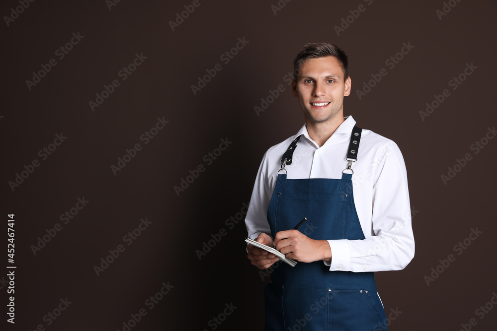 Portrait of happy young waiter with notebook on brown background, space for text Portrait of happy young waiter with notebook on brown background, space for text