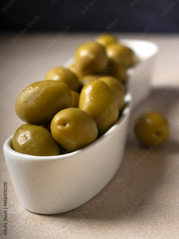 Green olives in a ceramic plate for snacks, dark background. Green olives in a ceramic plate for snacks, dark background.