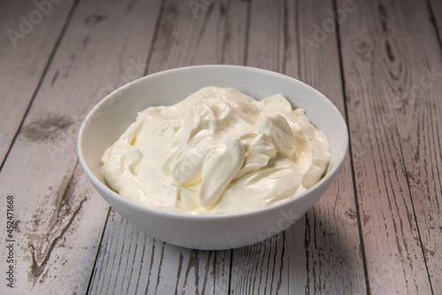 Whipped cream in a white bowl, Dairy product, healthy eating theme, wooden table background. High quality photo