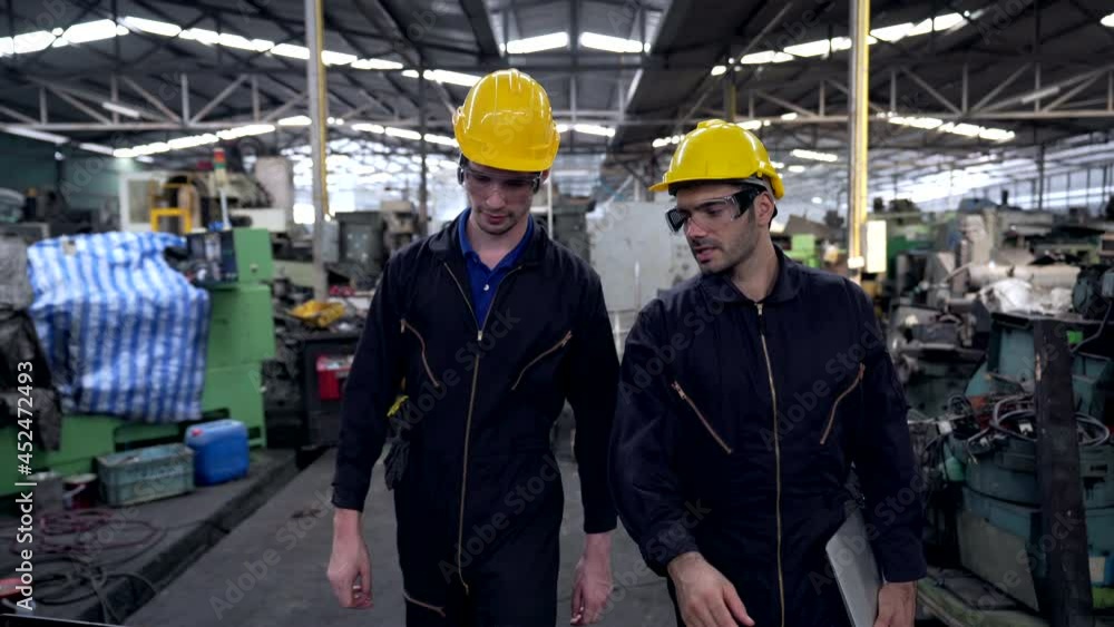 4K Two Caucasian man industry engineer team in safety helmet walking and working together in factory. Male foreman technician colleague using laptop computer working in metal manufacturing machine. 4K Two Caucasian man industry engineer team in safety helmet walking and working together in factory. Male foreman technician colleague using laptop computer working in metal manufacturing machine.