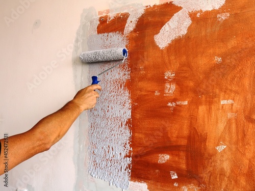 a roller in the hand of a painter painting a textured room wall, repainting the wall surface from bright brown to calm gray, painting the room wall with a roller plus copy space photo