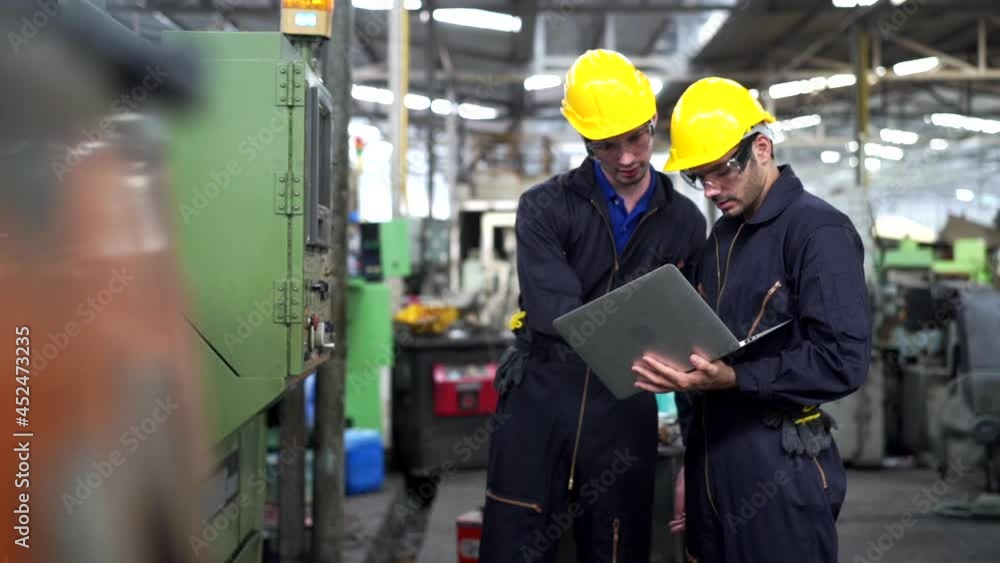 4K Two Caucasian man industry engineer team in safety helmet walking and working together in factory. Male foreman technician colleague using laptop computer working in metal manufacturing machine. 4K Two Caucasian man industry engineer team in safety helmet walking and working together in factory. Male foreman technician colleague using laptop computer working in metal manufacturing machine.