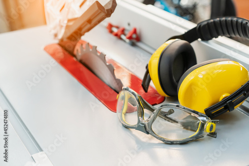 Safety glasses and Earmuffs on Electric saw table in workshop .Work safety concept . selective focus