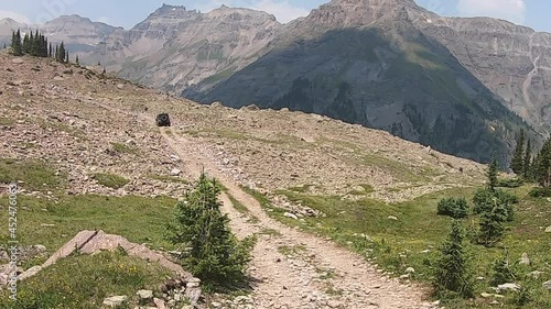 Following 4WD vehicle driving on trail across rocky plateau in the Yankee Boy Basin in San Juan Mountains in Colorado; view of Mt Sneffles; concepts of adventure, exploration and mountain landscape photo