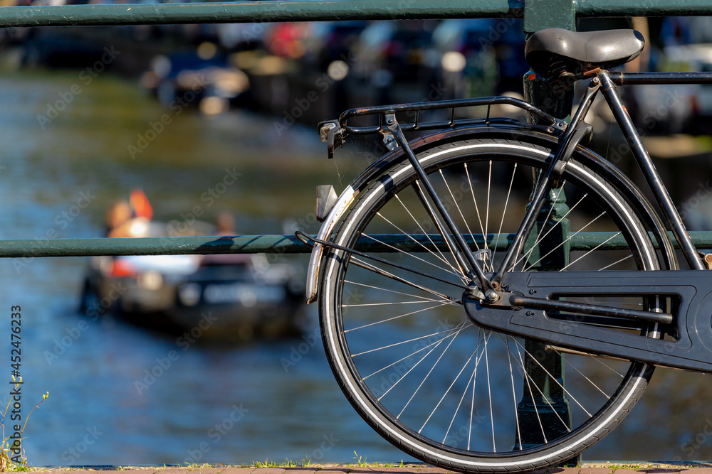 Fototapeta premium Selective focus of bicycle back wheel and seat with blurred of canal cruise boat as background, Old vintage bike with rust parked on canal bridge in Amsterdam, Netherlands land of bicycles.
