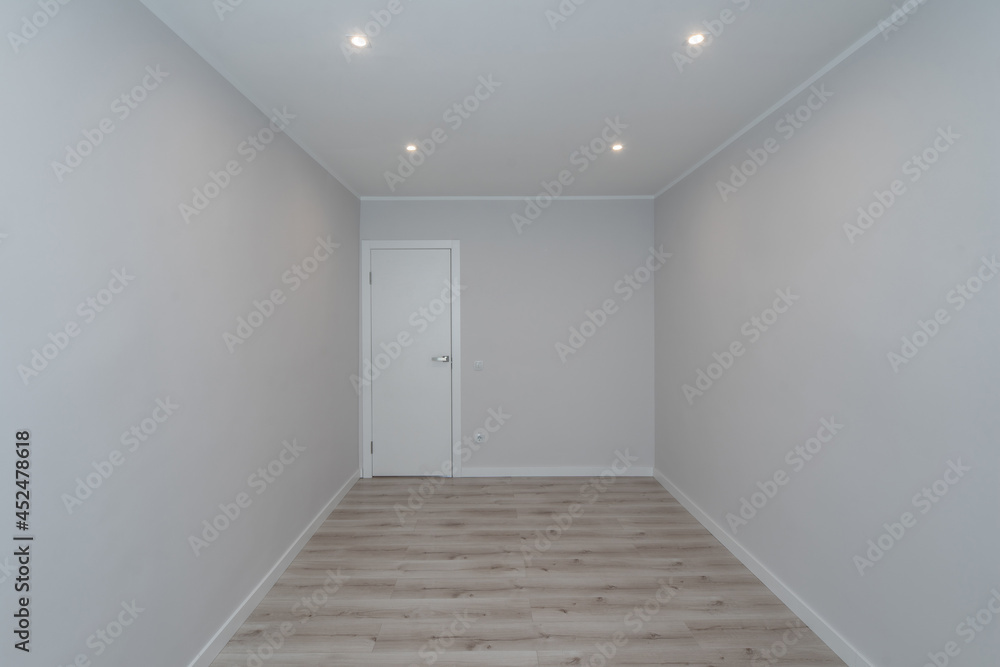 Obraz premium Contemporary interior of room in luxury renovated apartment. White walls. Parquet floor. Front view of wall with closed door.