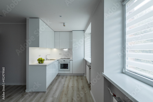Modern interior of renovated studio apartment without furniture. Front view of white kitchen with fridge and oven.