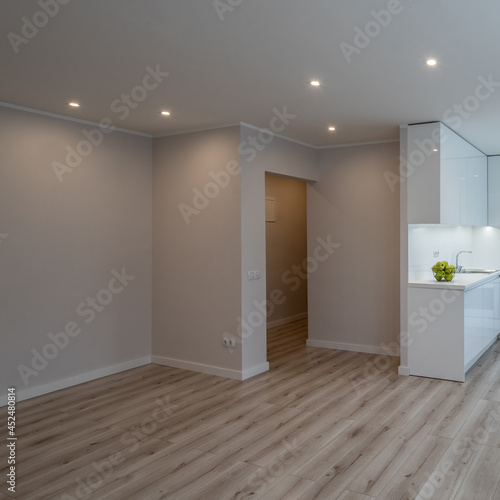 Bright interior of contemporary renovated apartment. White kitchen with fridge and oven. Parquet floor.