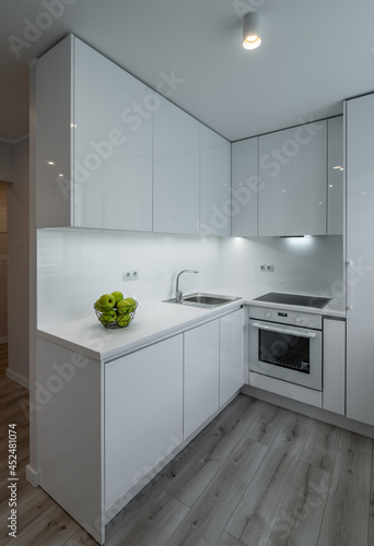 Modern interior of luxury studio apartment after renovation. White kitchen with fridge and oven. Living room without furniture.