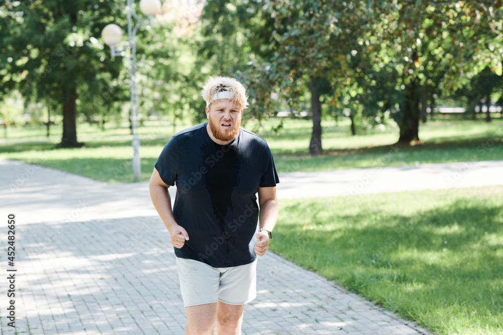 Overweight man in sports clothing jogging alone during training in the park Overweight man in sports clothing jogging alone during training in the park