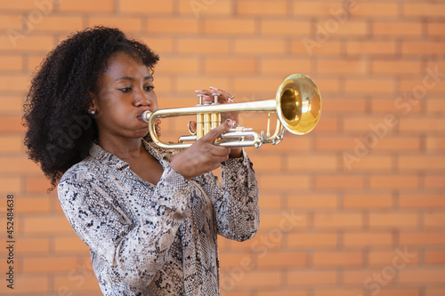 Portrait of a young afro american woman playing the trumpet outside on a brick wall background