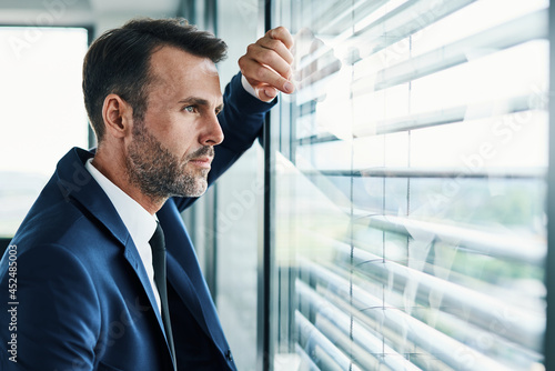 Thoughtful businessman looking through office window photo